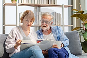 Portrait of happy senior couple in living room, Elderly woman and a man reading a book on cozy sofa at home, Happy family concepts