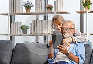Portrait of happy senior couple in living room, Elderly woman and a man using tablet smartphone on cozy sofa at home, Happy family