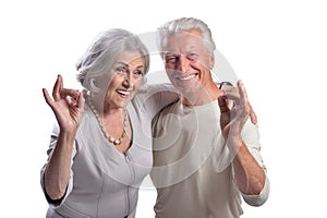 Portrait of happy senior couple showing ok on white background