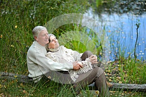 Portrait of happy senior couple sitting by pond