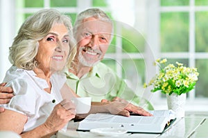 Portrait of happy senior couple sitting at table and reading book