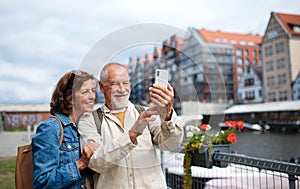 Portrait of happy senior couple tourists doing selfie outdoors in historic town