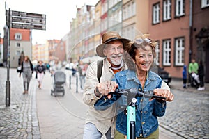 Portrait of happy senior couple tourists riding scooter together outdoors in town