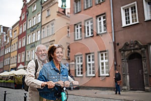 Portrait of happy senior couple tourists riding scooter together outdoors in town