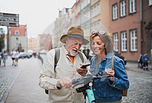 Portrait of happy senior couple tourists riding scooter together outdoors in town