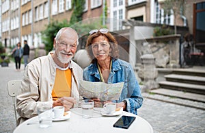 Portrait of happy senior couple tourists sitting and using map outdoors in town, looking at camera.