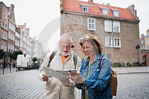 Portrait of happy senior couple tourists using map outdoors in town street