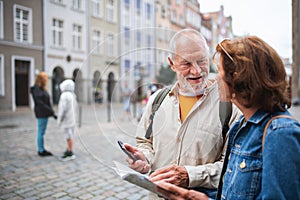 Portrait of happy senior couple tourists using map and smartphone outdoors in town street