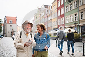 Portrait of happy senior couple tourists using smartphone outdoors in historic town