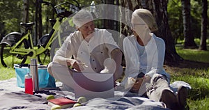 Portrait of happy senior couple using laptop relaxing on picnic outdoors.