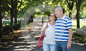 Portrait of happy senior couple walking outdoors in city or town park.