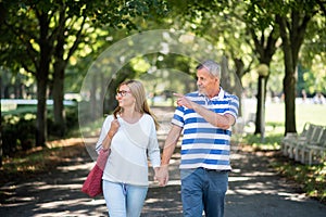 Portrait of happy senior couple walking outdoors in city or town park.