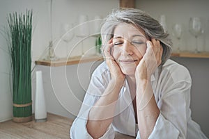 Portrait of a happy senior elderly woman with closed eyes in a bright comfortable apartment.