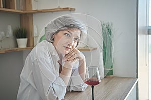 Portrait of a happy senior elderly woman with glass of wine in a bright comfortable apartment