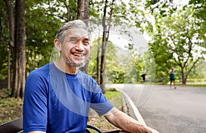 portrait happy senior man in sportswear sitting on bench in the forest park