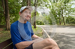 portrait happy senior man in sportswear sitting on bench in the forest park after running