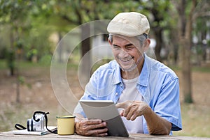 portrait happy senior man using online internet tablet searching direction for his journey while resting in the national park