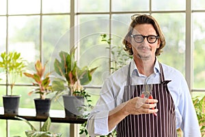 Portrait of happy senior man wearing glasses and denim apron holding pruner in home gardening. looking at camera