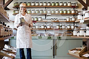 Portrait of a happy senior merchant standing with spice jar in store