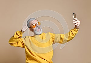 Portrait of happy senior millionaire man using smartphone cellphone make selfie in yellow sunglasses