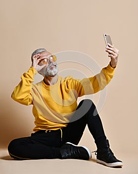 Portrait of happy senior millionaire man using smartphone cellphone make selfie in yellow sunglasses