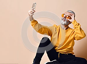 Portrait of happy senior millionaire man using smartphone cellphone make selfie in yellow sunglasses