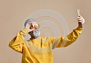 Portrait of happy senior millionaire man using smartphone cellphone make selfie in yellow sunglasses