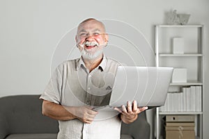 Portrait of happy senior office worker with a laptop. Senior man with a gray beard has a job in laptop at home office