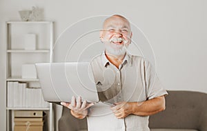 Portrait of happy senior office worker with a laptop. Senior man with a gray beard has a job in laptop at home office