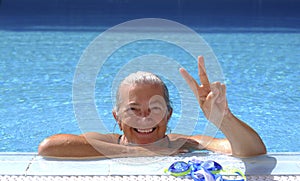 Portrait of an happy senior sporty woman enjoying swimm into the swimming pool doing ok gesture with hand  - active retiree