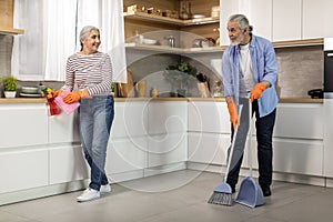 Portrait Of Happy Senior Spouses Making Cleaning In Kitchen Together