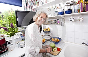 Portrait of happy senior woman chopping fresh vegetables at kitchen counter