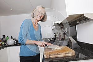 Portrait of happy senior woman chopping vegetables at kitchen counter