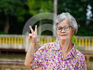 Portrait of happy senior woman hand showing victory sign, smiling, and looking at the camera. Concept of aged people