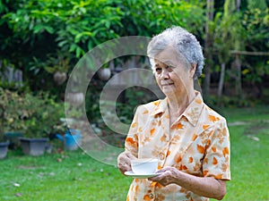 Portrait of a happy senior woman holding a white coffee cup while standing in the garden. Space for text. Concept of aged people