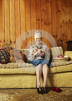 Portrait of happy senior woman knitting on sofa at home