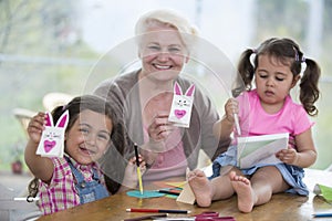 Portrait of happy senior woman showing craft rabbit while sitting with granddaughters at home