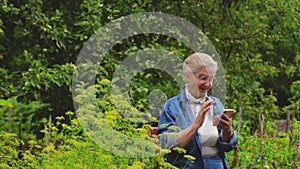 Portrait happy senior woman sitting in park and using smartphone or phone in hands. Mature female uses app in gadget in