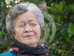 Portrait of a happy senior woman smiling and looking at the camera while standing against trees. Concept of aged people