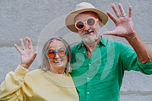 Portrait of happy seniors couple in colourful clothes waving at camera.
