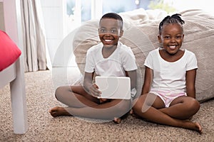 Portrait of happy siblings with digital tablet sitting on rug