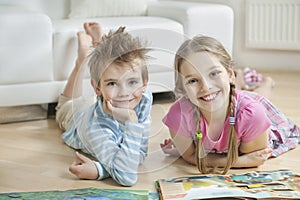 Portrait of happy siblings with story books lying on floor in living room