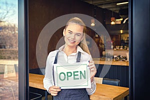 Portrait of happy small business owner standing at restaurant entrance holding open sign