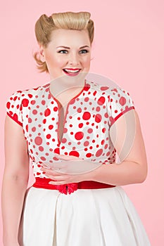 Portrait of happy smiled blonde woman with vintage pin-up make-up. Blonde female with curls isolated on pastel pink background