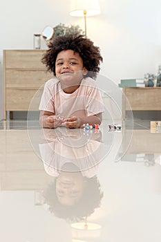 Portrait of happy smiling African boy with black curly hair lying on floor and playing toy in bedroom. Child with reflections on