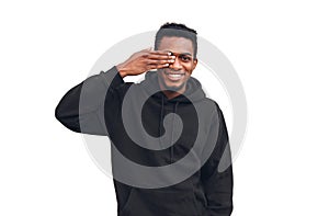 Portrait happy smiling african man closing face with hand and looking by one eye wearing black hoodie isolated on white