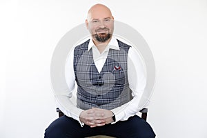 Portrait of happy smiling bald middle-aged businessman in grey vest, blue jeans, white shirt sitting on wooden chair.