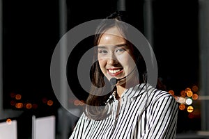 Portrait of happy smiling beautiful Asian woman with headphones work night shift at call center customer care service desk,