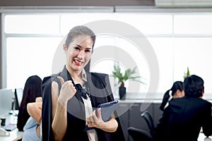 Portrait of happy smiling beautiful Asian woman officer holds tablet, standing at office with blurred background of busy working