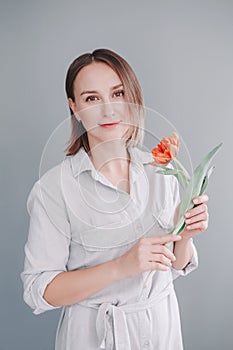 Portrait of happy smiling beautiful middle age Caucasian woman holding red tulip flower. Real woman with short hair at grey light